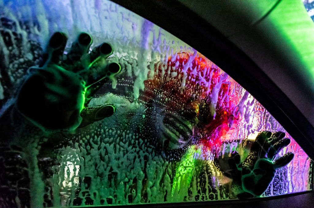 A scare actor presses his face up against a car window in a haunted car wash 