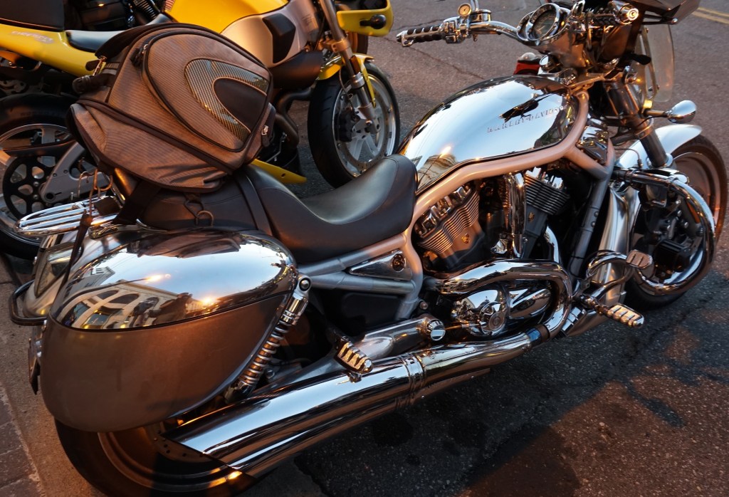 A chrome Harley-Davidson V-Rod parked on the street next to a yellow Buell