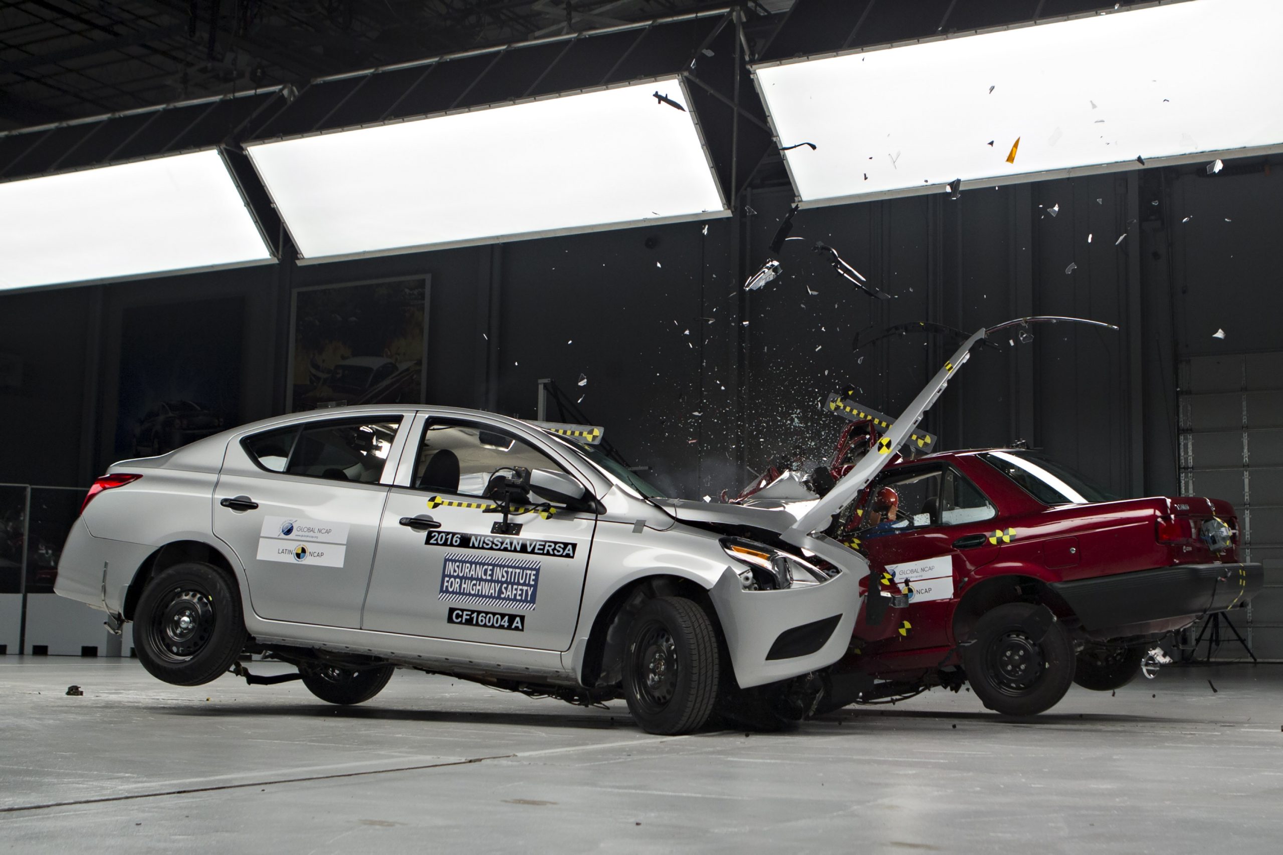 A silver Nissan Versa and a red car colliding during an IIHS crash test