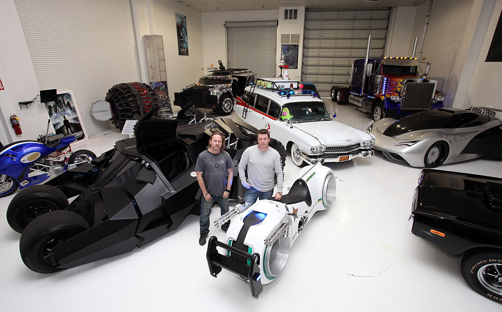Brothers Marc and Shannon Parker stand in the middle of a garage filled with replicas of famous cars from film. The bat-mobile, Ghostbusters station wagon and  a light cycle as featured in tron stand out