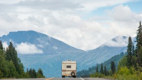 An RV drives down the road with mountains in the background
