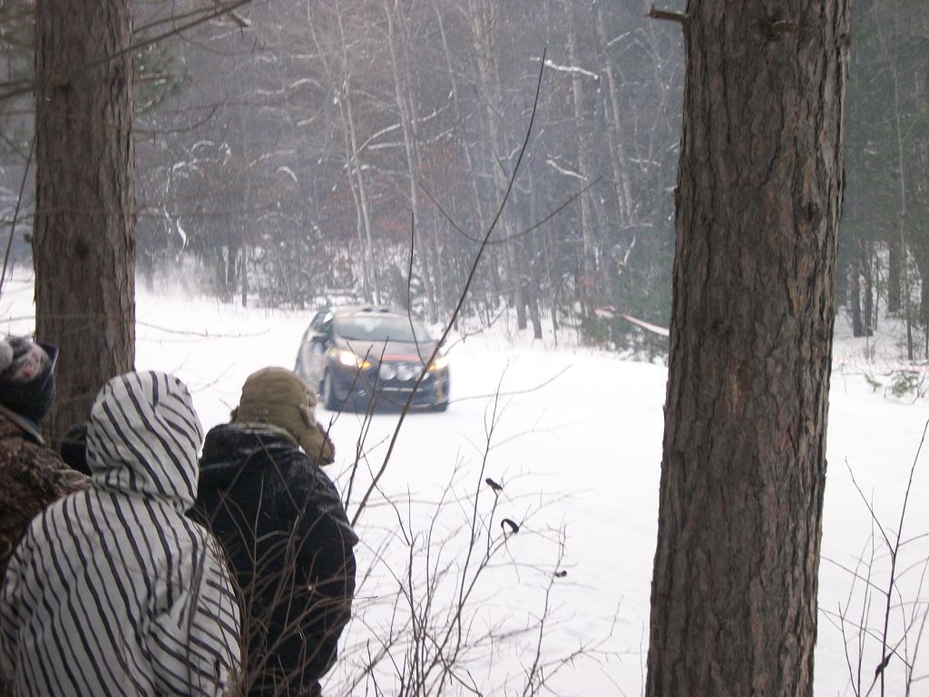 Race spectators in coats and hats at a snowy 2017 SnoDrift Rally forest stage