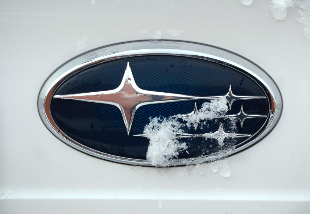 A snow-covered oval shaped Subaru logo on a white vehicle. 