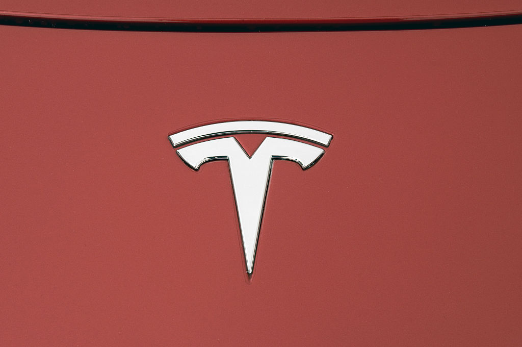 A silver Tesla logo on a red vehicle hood