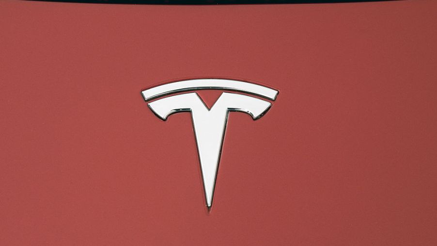 A silver Tesla logo on a red vehicle hood