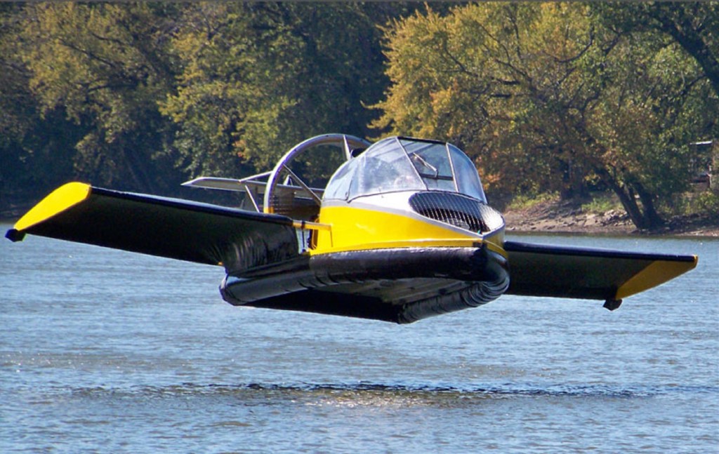 A yellow-and-black Universal Hovercraft 19XRW Hoverwing hovering over a river