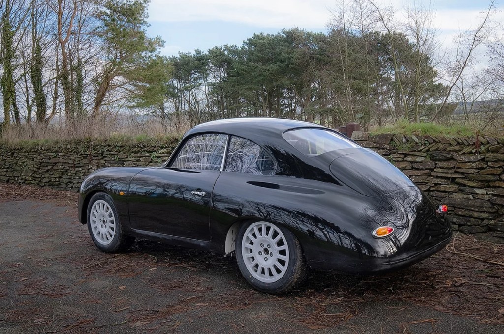 The rear 3/4 view of a black WEVC Coupe development prototype on a hedge-lined road