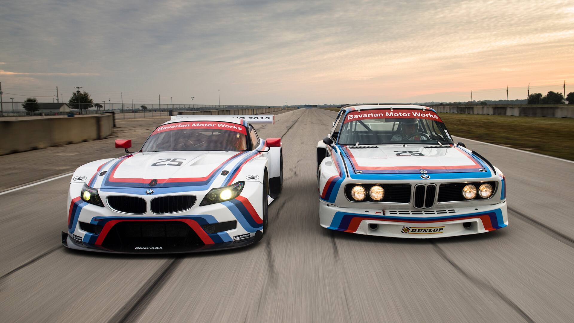 A new BMW M car and heritage BMW M car, both white with iconic red, purple and blue stripes