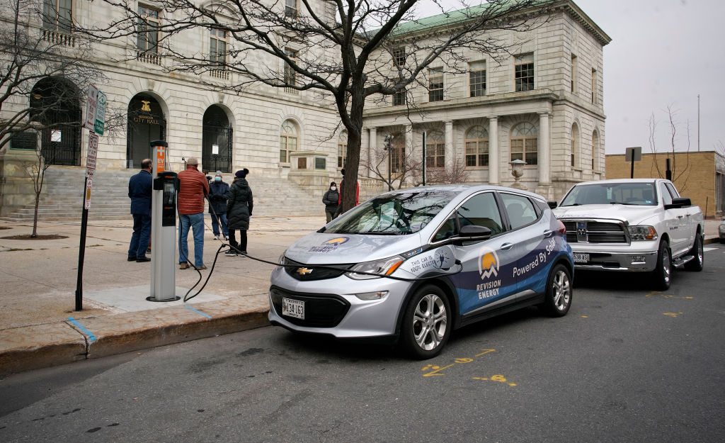 A chevy bolt attached to a charging station parked on the side of the road