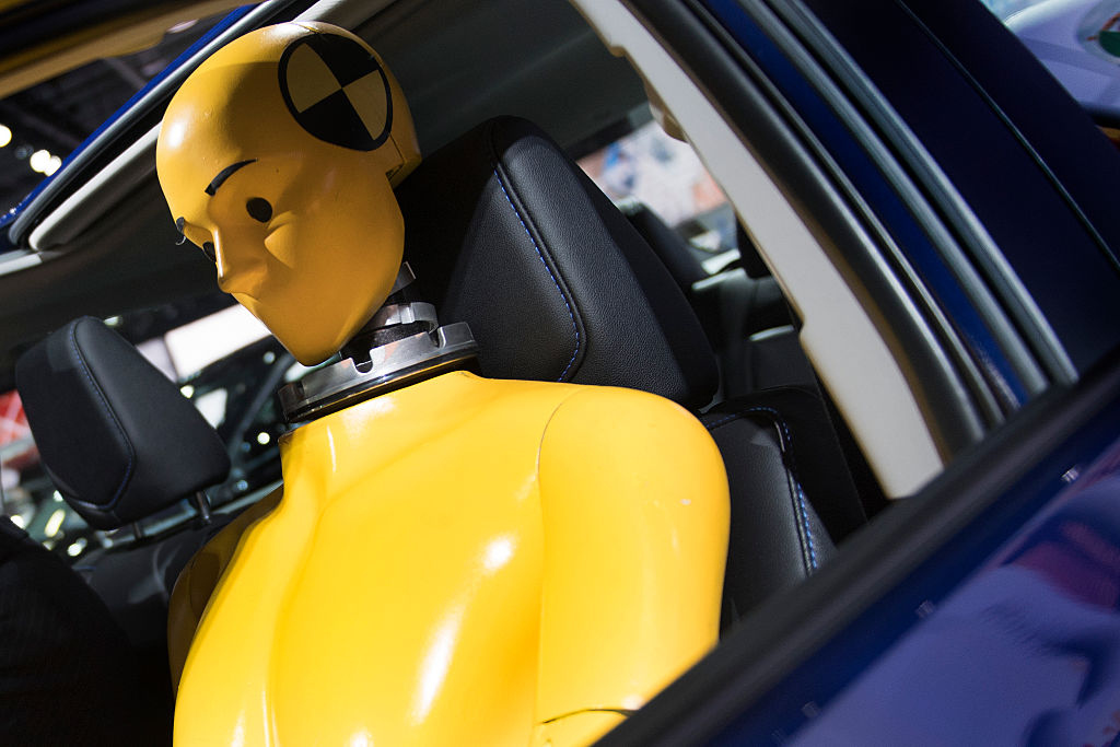 Close up through the driver's window of a yellow crash test dummy seated in a blue car
