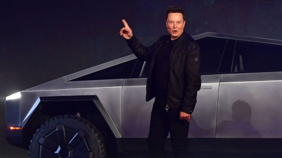 Tesla CEO Elon Musk points upward as he stands in front of a stainless steel Cybertruck