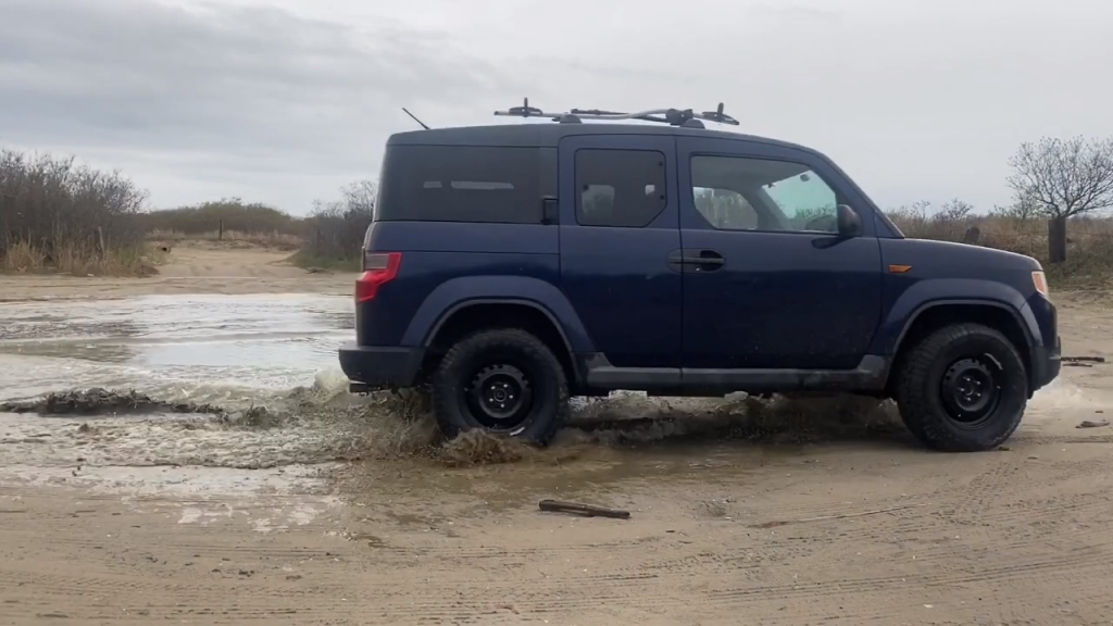 A lifted 2009 Honda Element drives through the mud 