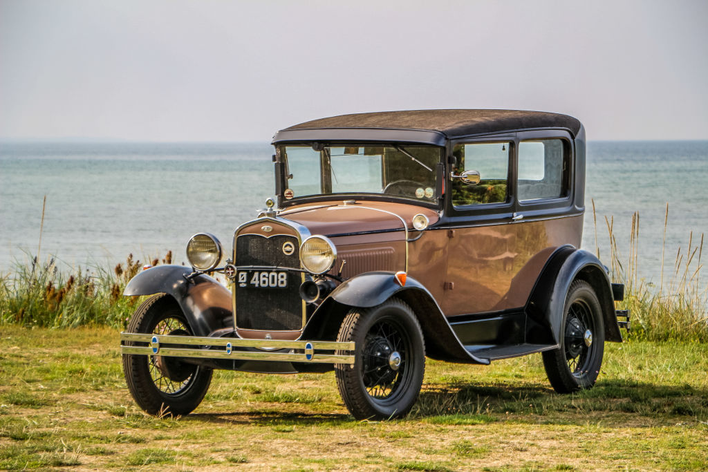 A brown Model A Ford, classic getaway car, parked on a grassy sea-side cliff