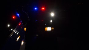 A police car with red and blue lights behind a motorist's vehicle during a traffic stop at night