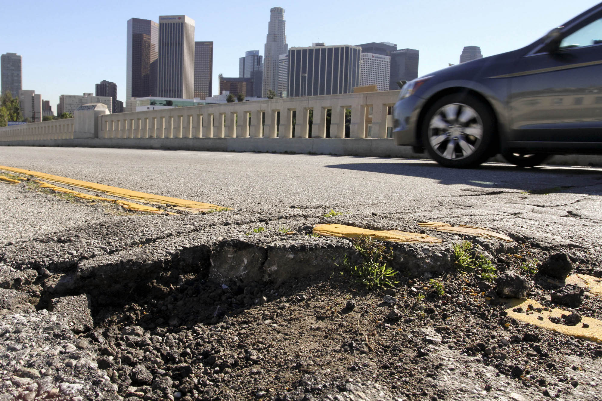 A car drives past potholes and broken asphalt on a road in Los Angeles, California, on Friday, January 21, 2011