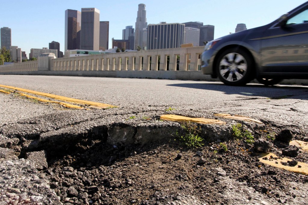 A car drives past potholes and broken asphalt on a road in Los Angeles, California, on Friday, January 21, 2011
