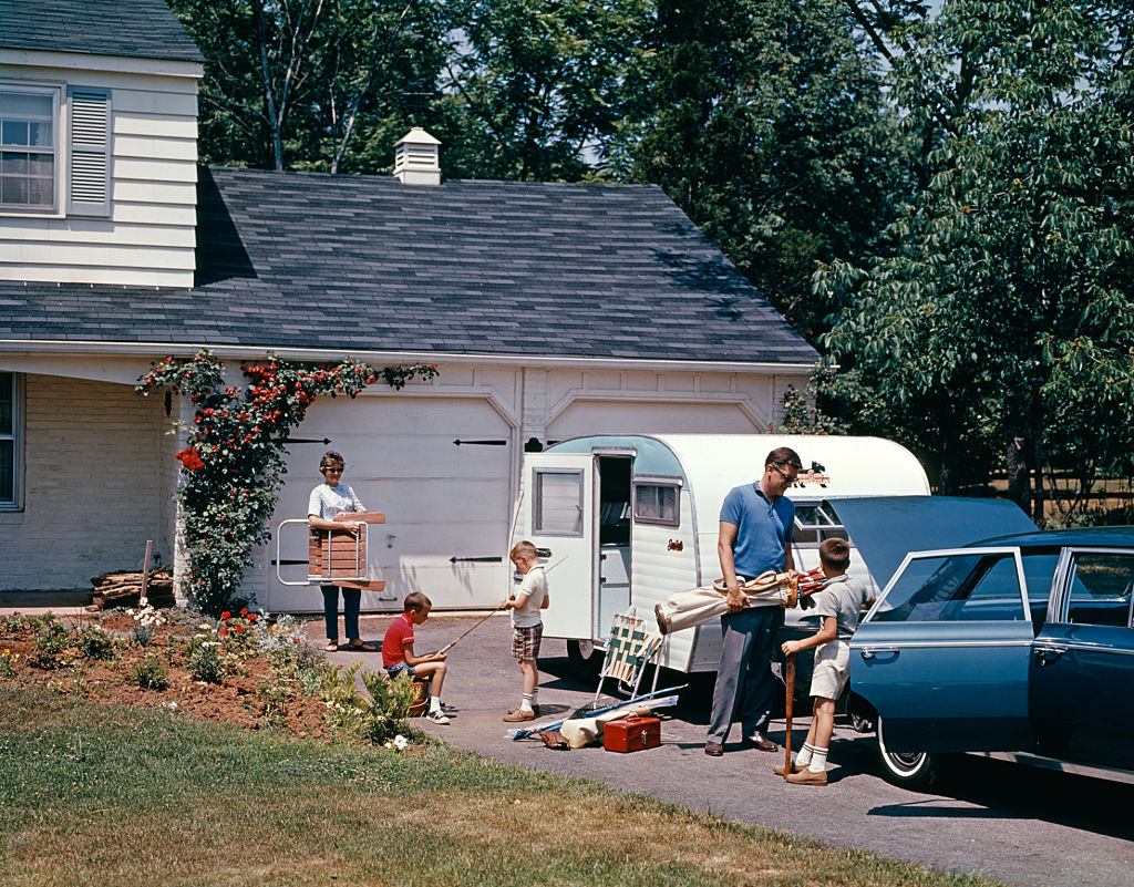 A 1960s family packing their vehicle and camper for a road trip