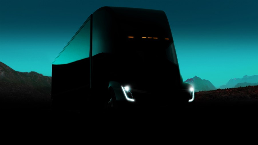 A dark photo of a Tesla Semi truck concept vehicle with its headlights on in front of mountains