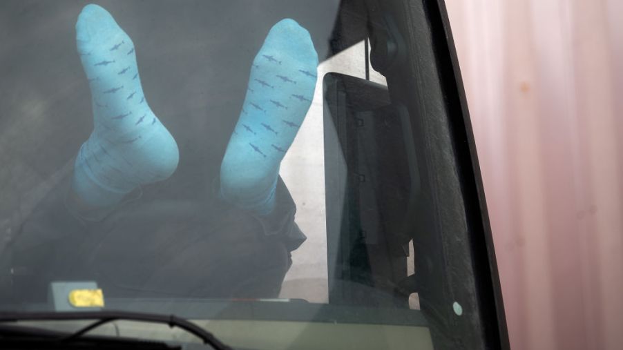 A trucker driver rests his feet on the dashboard as he rests