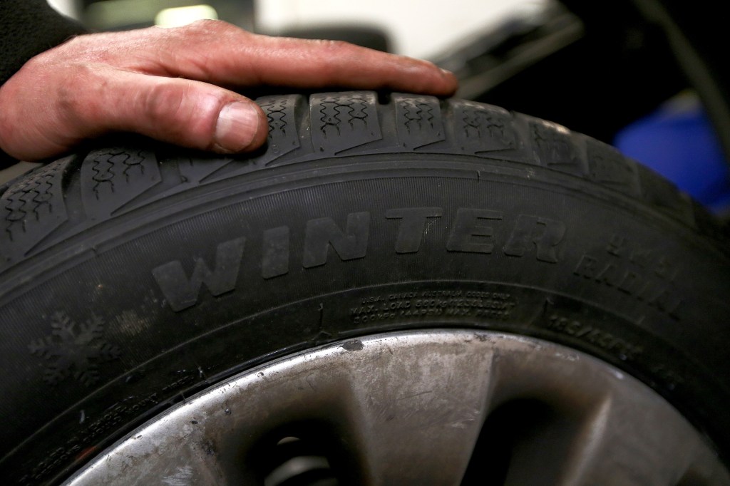 A car mechanic holds a winter tire at a garage. 