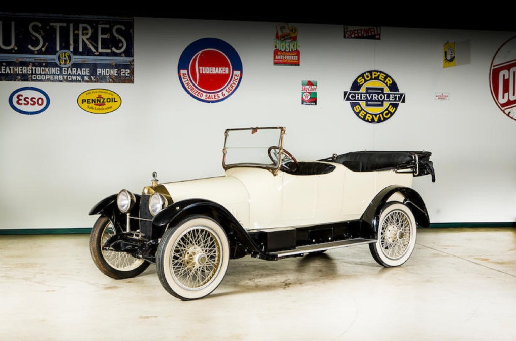 A white 1916 Owen Magnetic Tourer in a garage with various car logos