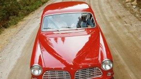 A red 1961 Volvo Amazon drives down a dirt road