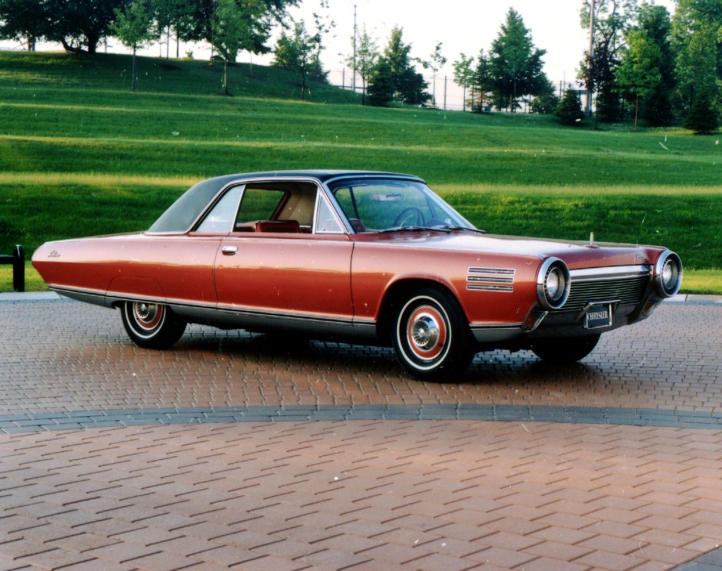An orange 1963 Chrysler Turbine parked on a brick driveway by a lawn