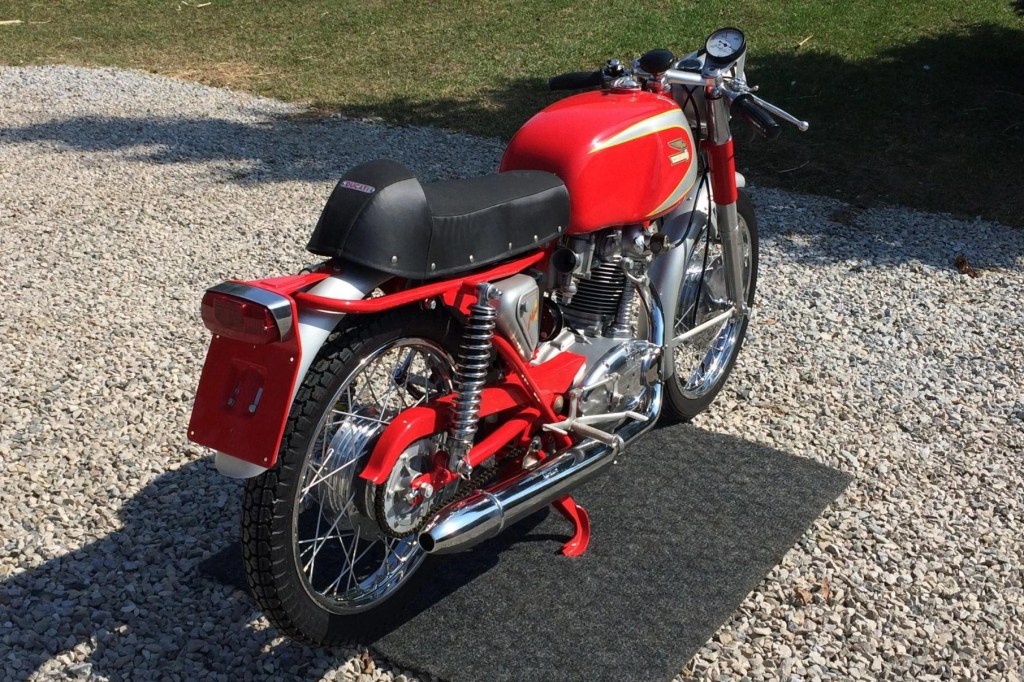 The rear 3/4 view of a red-and-silver 1965 Ducati Mach 1 on a gravel driveway