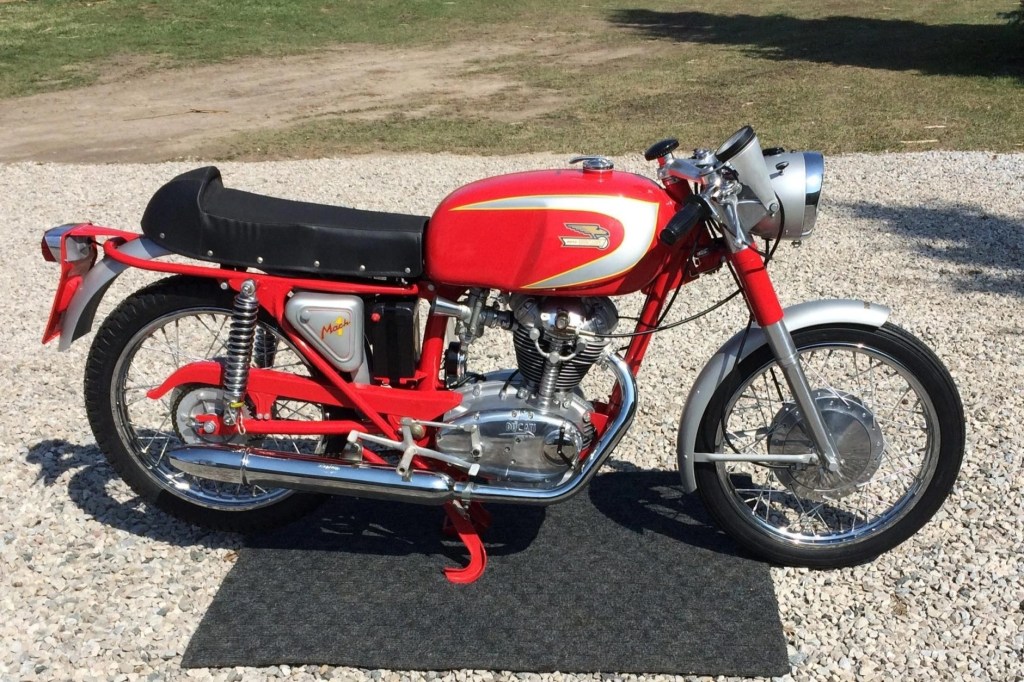 The side view of a red-and-silver 1965 Ducati Mach 1 on a gravel driveway
