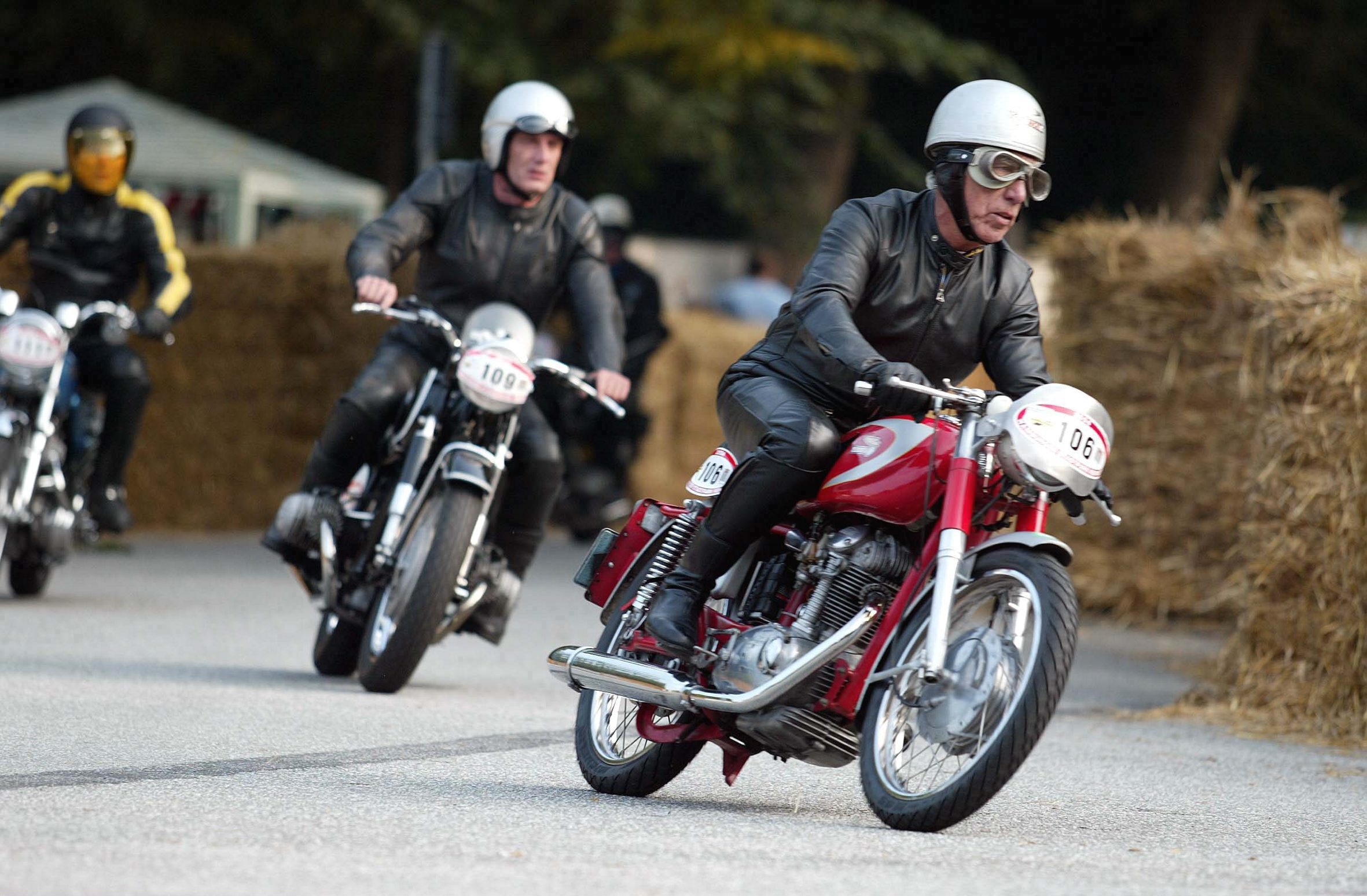 A black-clad rider on a red-and-silver 1967 Ducati Mach 1 leads 1966 BMW R50 and 1969 Norton Commando at a 2004 Hamburg, Germany race