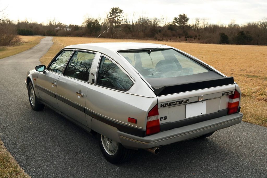 The rear 3/4 view of a silver 1986 Citroen CX 25 Prestige Turbo on a winding road