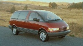 A red 1991 Toyota Previa minivan parked on a rural road with hills in the background