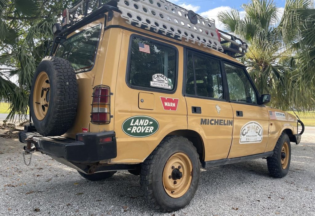 The rear 3/4 view of a yellow 1992 Land Rover Discovery Camel Trophy on a sandy beach