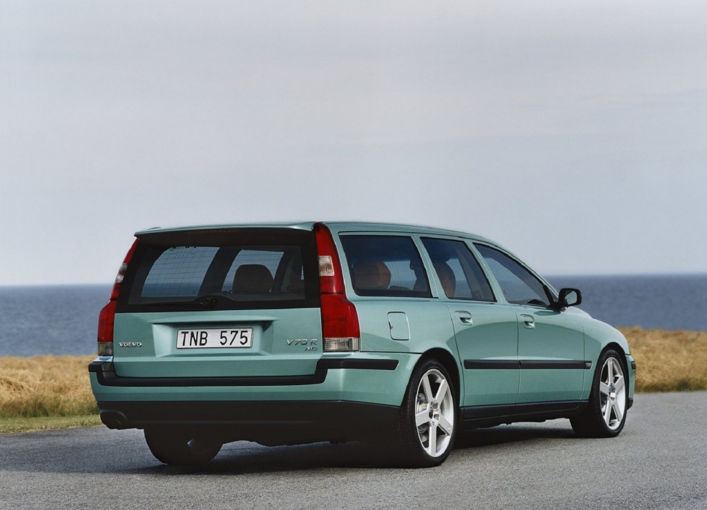 The rear 3/4 view of a teal 2003 Volvo V70R parked by a body of water