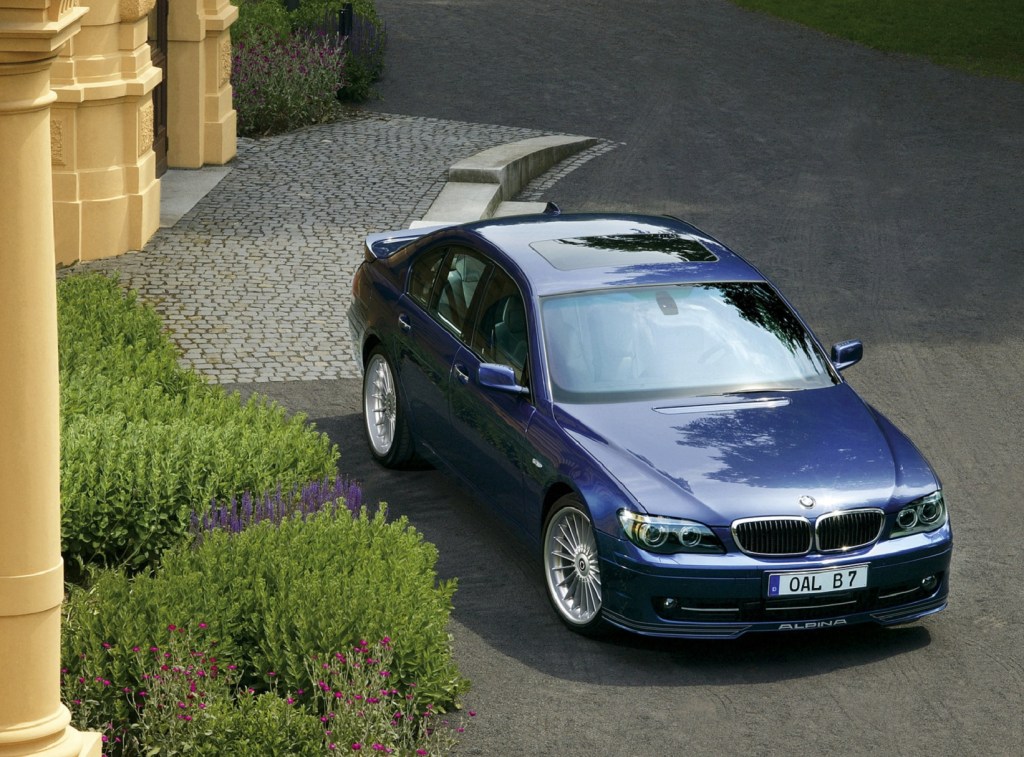 An overhead front 3/4 view of a blue 2007 BMW Alpina B7 in front of a yellow villa