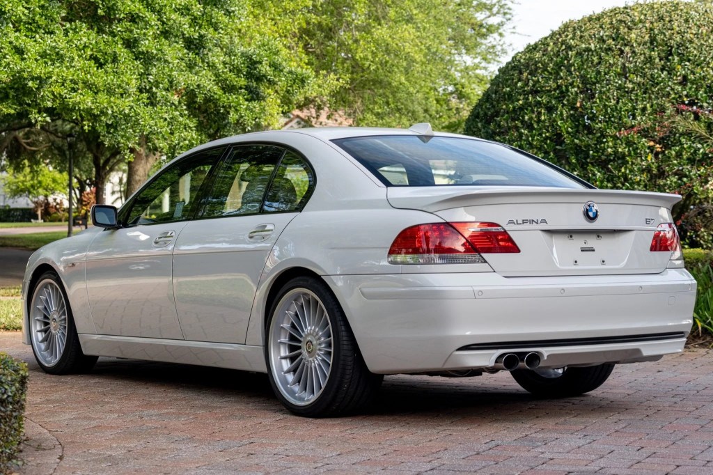 The rear 3/4 view of a white 2007 BMW Alpina B7 parked on a bush-lined driveway