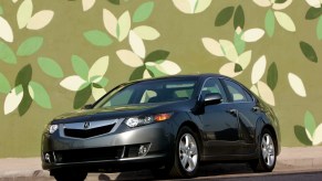 A dark-gray metallic 2008 Acura TSX sports sedan parked in front of a green leaf background