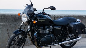 A black 2009 Triumph Bonneville with saddlebags parked by a beach-side stone wall