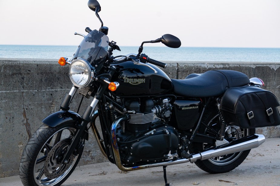 A black 2009 Triumph Bonneville with saddlebags parked by a beach-side stone wall