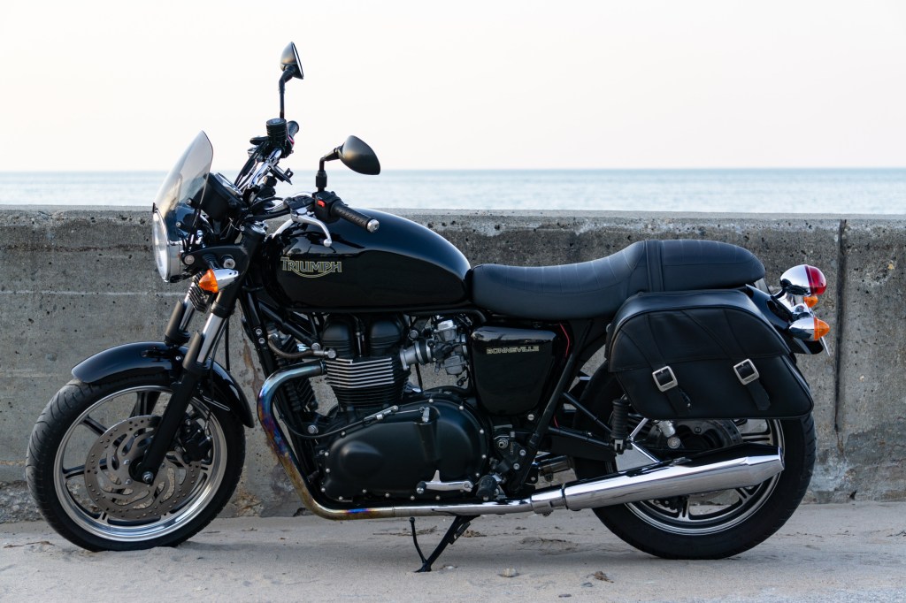 The side view of a black 2009 Triumph Bonneville with saddlebags next to a beach-side concrete wall