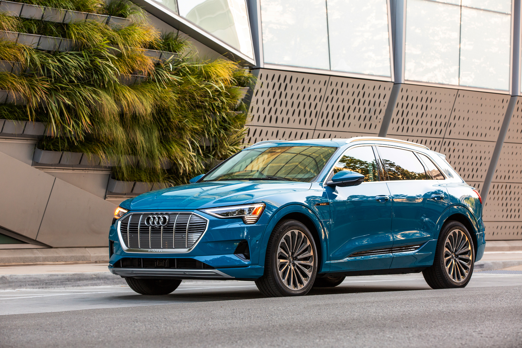 A bright-blue 2019 Audi e-tron electric crossover SUV parked on a street outside a modern building