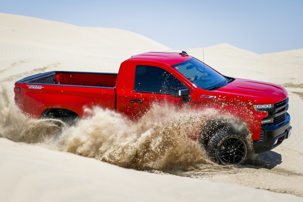 a red Chevy Silverado short bed, single cab pickup kicking up sand on the dunes