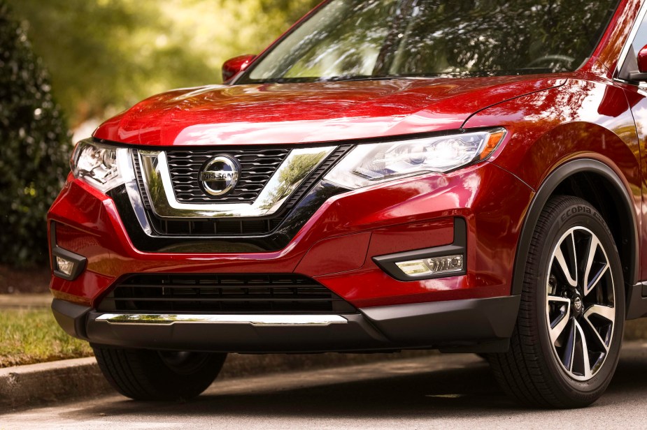 A red metallic 2019 Nissan Rogue compact crossover SUV parked next to a curb