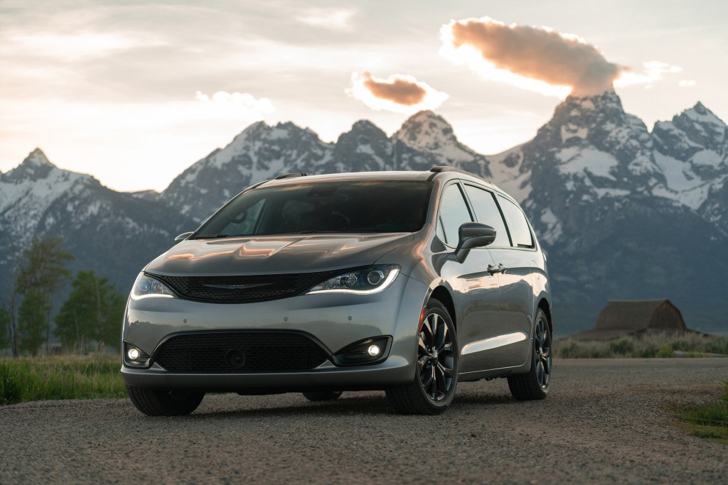 A silver 2020 Chrysler Pacifica Limited minivan parked on gravel in front of snowcapped mountain with the sun behind them