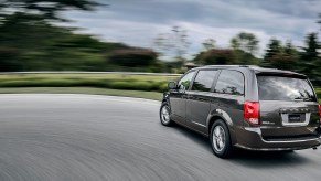 A dark-gray 2020 Dodge Grand Caravan minivan traveling on a road lined with green grass and trees