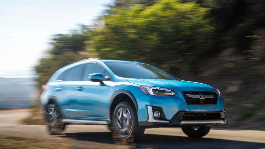 A sky-blue 2020 Subaru Crosstrek Hybrid crossover SUV traveling on a curving road near a large body of water on a sunny day