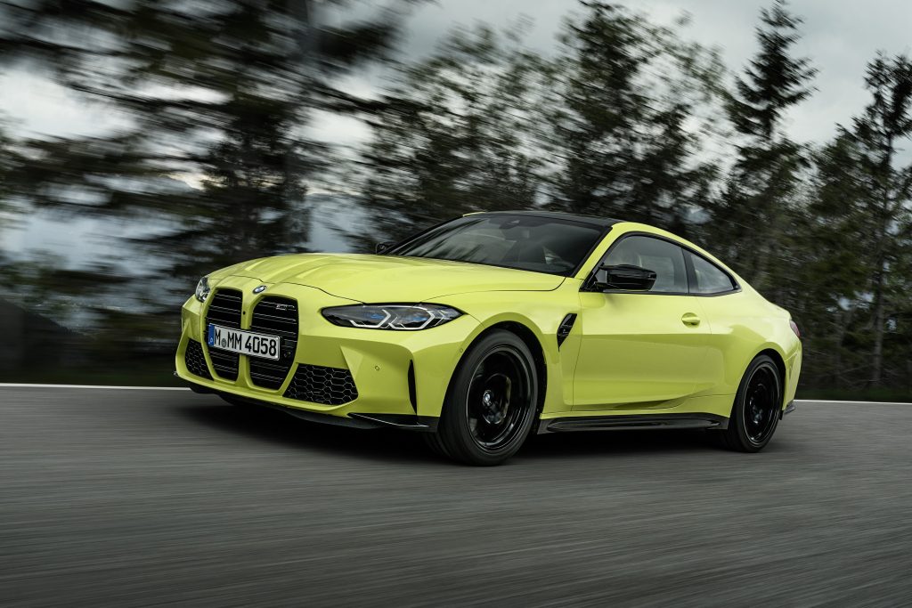 A yellow-green 2021 BMW M4 Competition driving on a forest-lined road