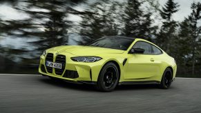 A yellow-green 2021 BMW M4 Competition driving on a forest-lined road