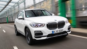A white 2021 BMW X5 midsize crossover luxury SUV travels on a covered road