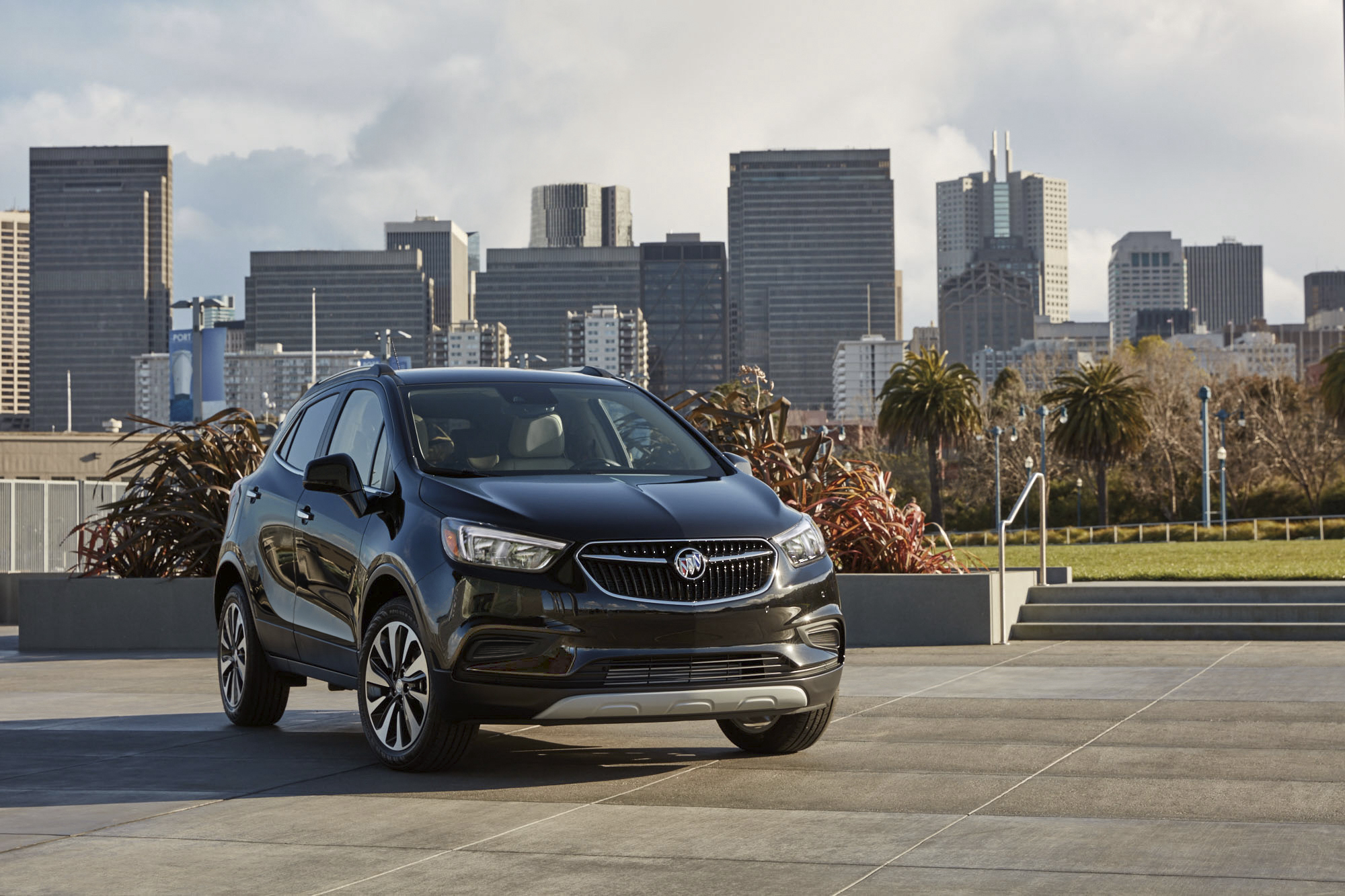 A dark-colored 2021 Buick Encore luxury subcompact SUV parked in front of a city skyline